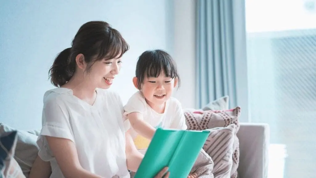 親子で楽しむ絵本時間|笑顔あふれるリビングでの読み聞かせ | my stellaマイステラブログ|子どもの好きが育つヒントと親子の時間 明るいリビングで、母親が娘と一緒に絵本を楽しそうに読み聞かせしている様子。
