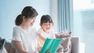 明るいリビングで、母親が娘と一緒に絵本を楽しそうに読み聞かせしている様子。