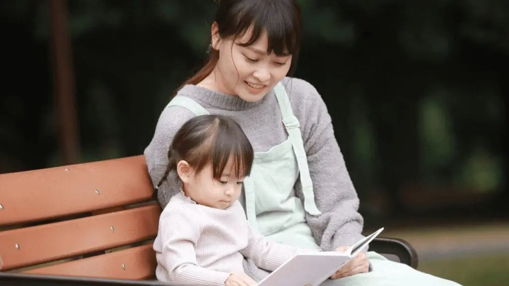 公園のベンチで読み聞かせを楽しむ母と娘|my stella | my stellaマイステラブログ|子どもの好きが育つヒントと親子の時間 公園のベンチで母親が幼い女の子に絵本を読み聞かせている様子。親子の穏やかなひととき。