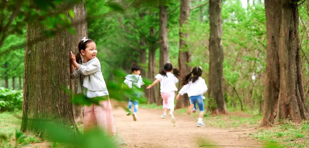 公園で忍者になりきりかくれんぼ遊びをする子どもたち | 出産祝い誕生日のプレゼントに家族みんなのパーソナライズ絵本|マイステラ 公園の木立の中で忍者ごっこをして遊ぶ子どもたち。木に隠れながら走り回り、想像力をふくらませている様子