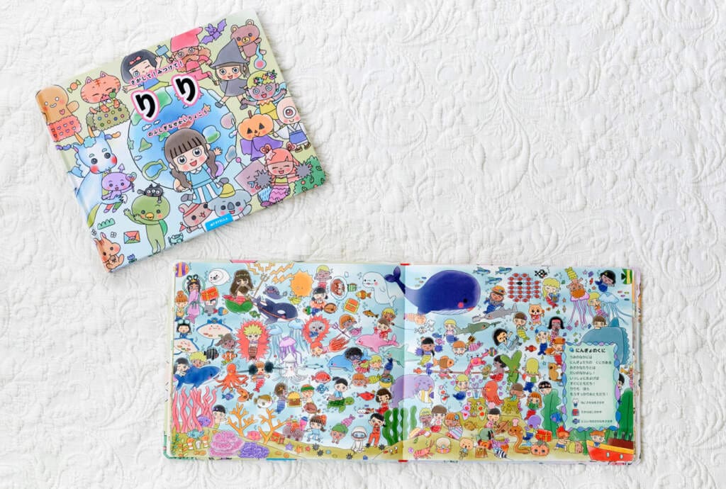MY STELLAの名前入り絵本『さがして！みつけて！ふしぎなせかいりょこう』の表紙に「りの」の名前が印刷され、開いたページには海の国の探し絵が描かれている。カラフルなキャラクターが散りばめられた「さがして！みつけて！」ゲームが楽しめる絵本。