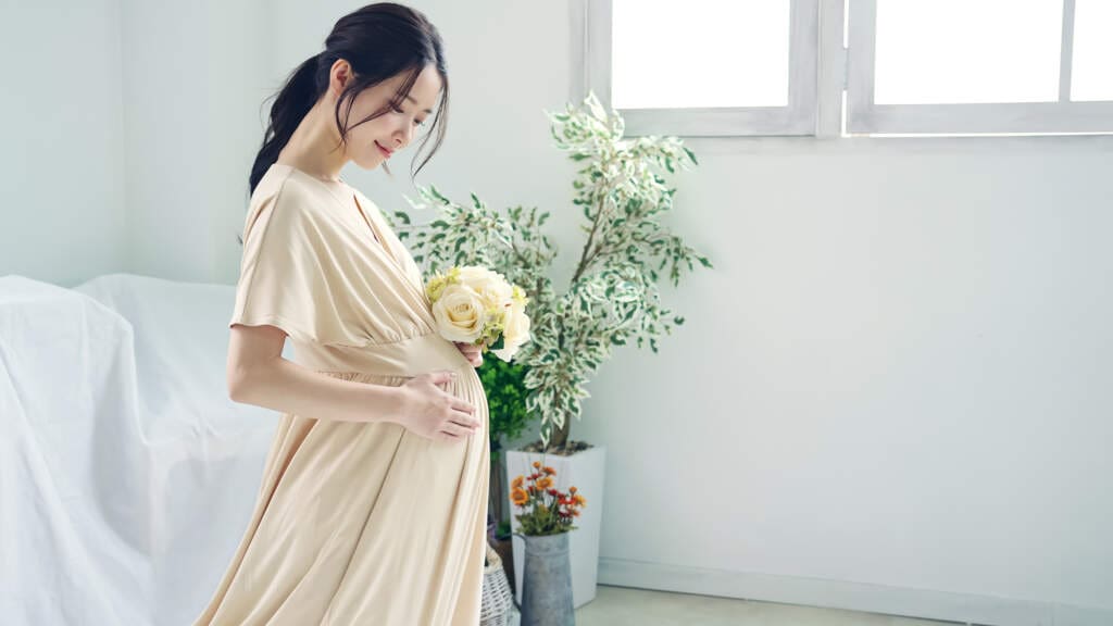 花束を持ち微笑む妊婦さん｜出産祝いに贈りたい心温まるギフトのイメージ