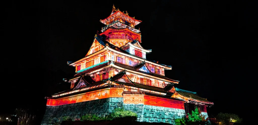 Iseninjakingdomnightprojectionmapping | 出産祝い誕生日のプレゼントに家族みんなのパーソナライズ絵本|マイステラ 三重県伊勢市のともいきの国 伊勢忍者キングダムの城郭を夜間にライトアップし、カラフルなプロジェクションマッピングを映し出している様子